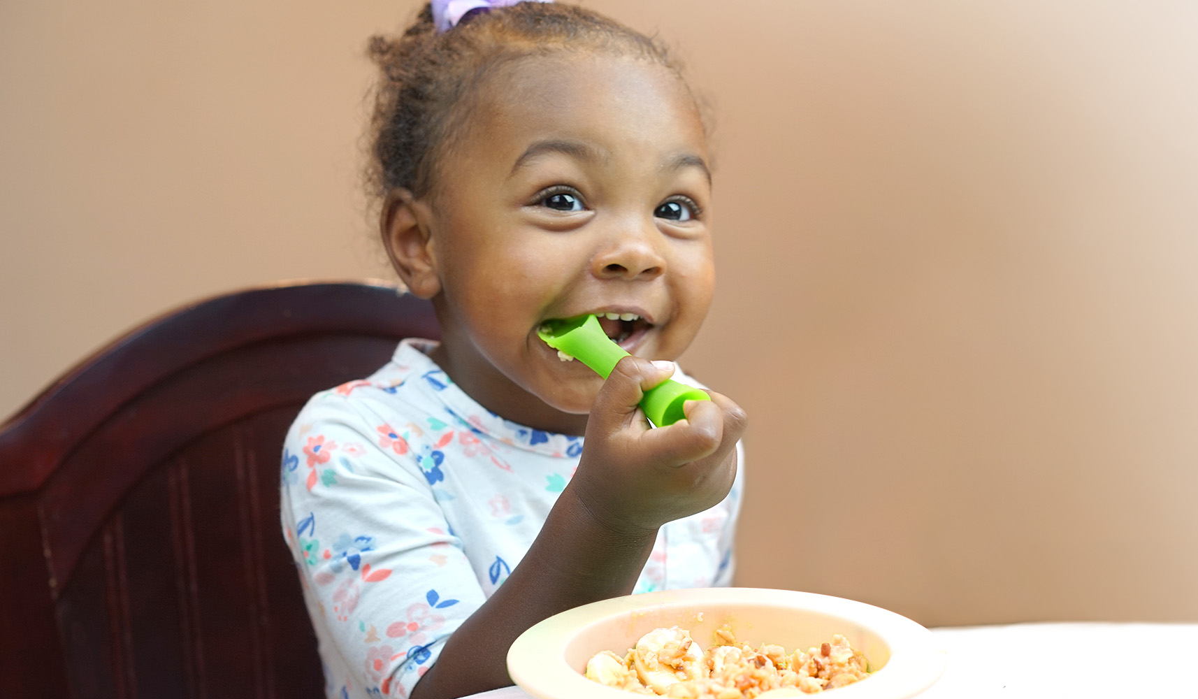 Un niño pequeño se sienta en una trona y come la comida de un plato con una  cuchara. utensilios de silicona para bebés para alimentar a los bebés